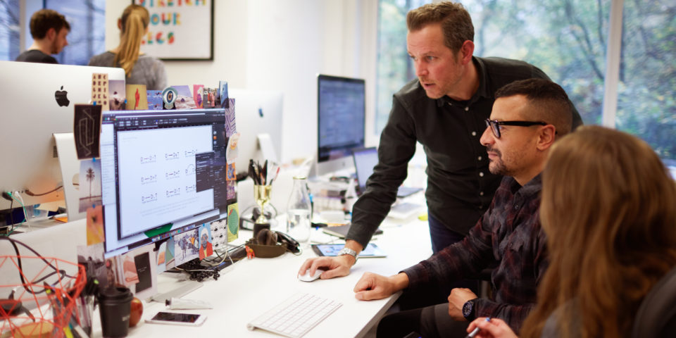 Three designers are looking at a computer screen in the Design102 office.