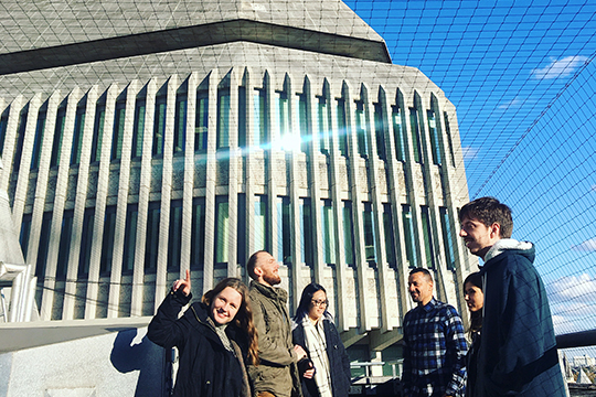 Six members of the Design102 team stand outside, in front of a concrete building.