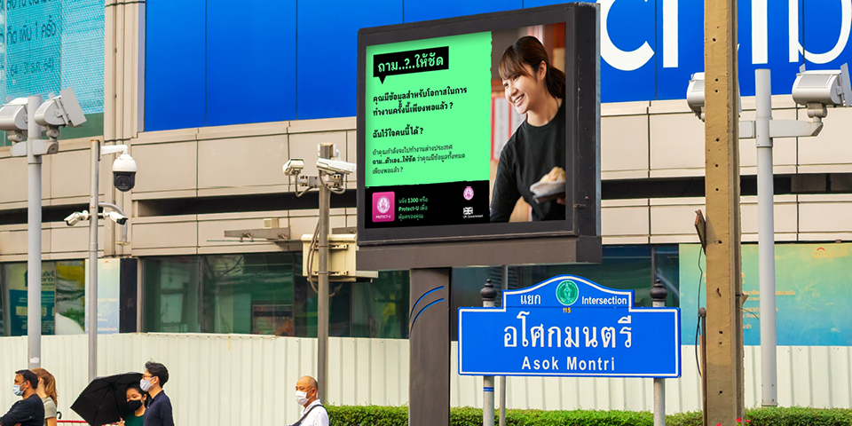 A billboard in Bangkok, Thailand, displays the campaign message alongside a picture of a smiling woman. The billboard is written in the Thai language.