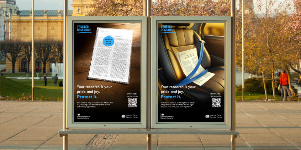 Two billboards in a bus station display two of the campaign posters. One shows a bubblewrapped document and the other shows a document strapped into a car seat. Both bear the headline 'you're research is your pride and joy. Protect it'.