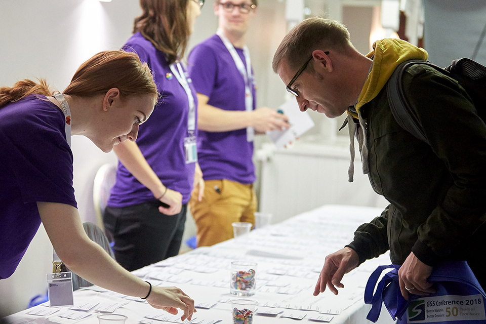 A woman working at the event helps an attendee find his name badge on a table.