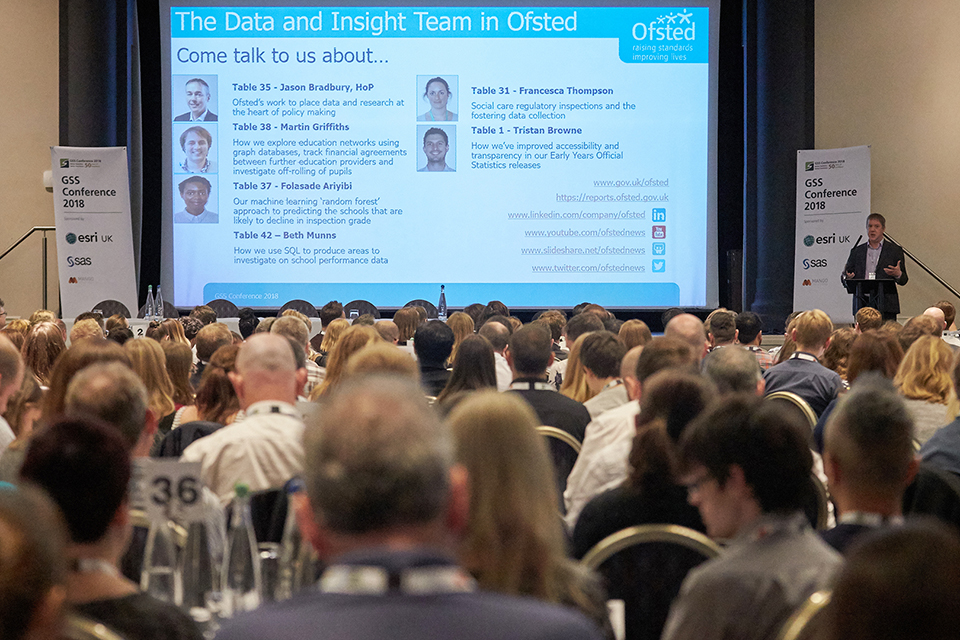 A speaker presents beside a large screen showing a slide titled 'The Data and Insight Team in Ofsted'. The photograph is taken from behind the audience.