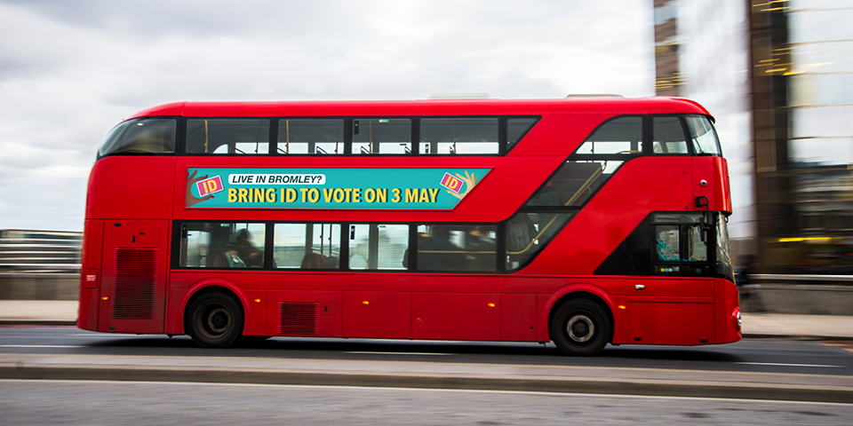 A red London bus is whizzing past. The advert on the side of the bus says: Live in Bromley? Bring ID to vote on 3rd May.