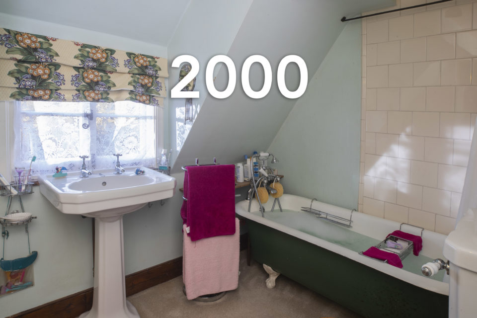 A family bathroom shows a free standing sink and bath full of water next to hanging pink towels, the year 2000 is written over the photo