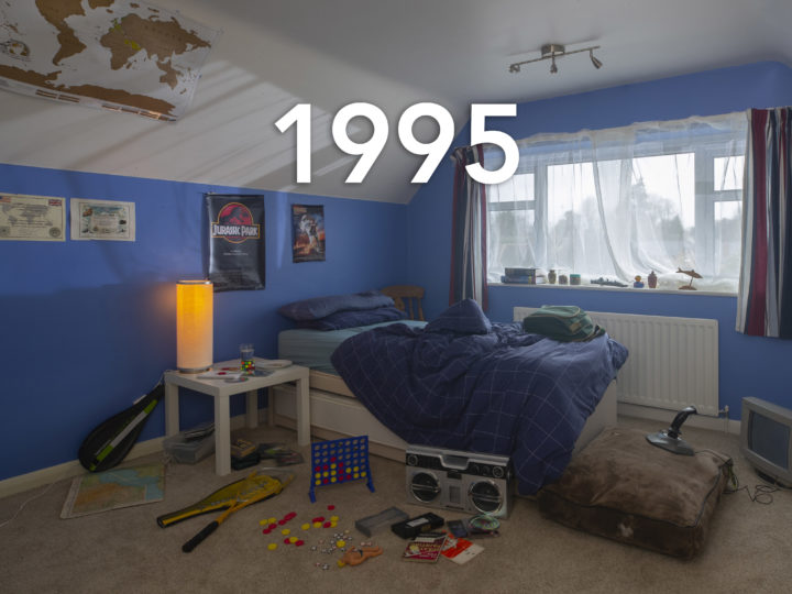 A classic 90s child's bedroom, toys surround an unmade bed and the walls are painted blue, the year 1995 is written over the photo