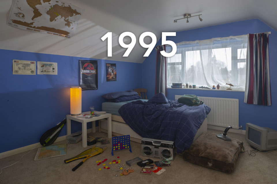 A classic 90s child's bedroom, toys surround an unmade bed and the walls are painted blue, the year 1995 is written over the photo
